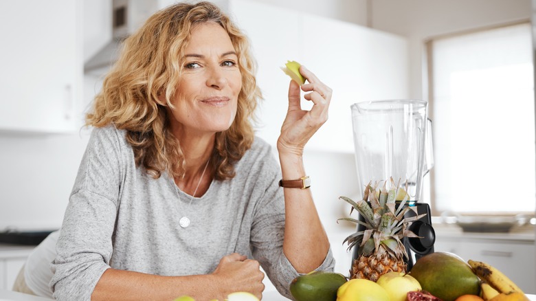 smiling mature woman eating fruits in kitchen