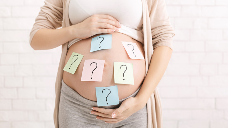 Pregnant woman holding her belly, which has post-its with question marks on them