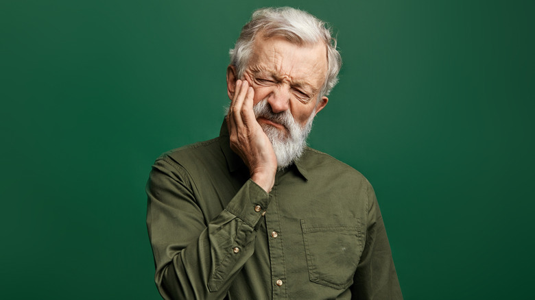 Man with white beard holding his face in discomfort
