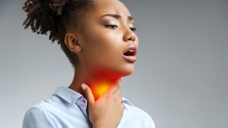 Woman in light blue shirt holding her sore throat