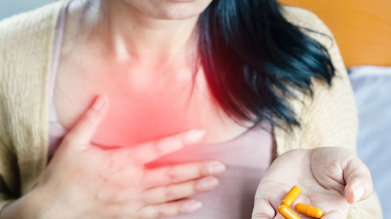 woman clutching her chest and holding pills acid reflux heartburn