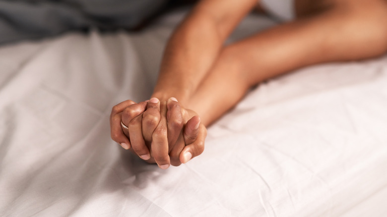 two people bed holding hands