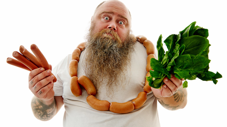 a man holding hot dogs in one hand and lettuce in the other looks conflicted about which to eat 