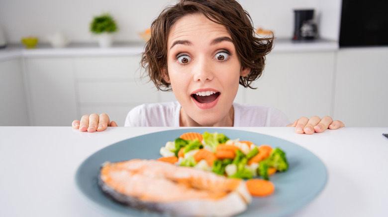 a woman stares wide eyed and open mouthed at a plate of food