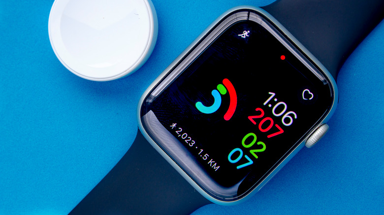 An Apple Watch Series 6 with the activity digital and a charger on a blue background.