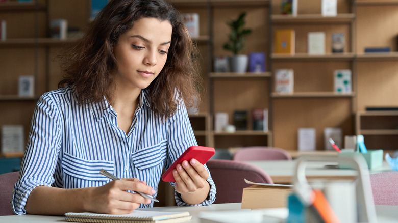 teen looking at her phone while sitting at a desk