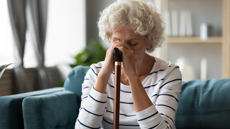 Older woman sits with her hands on cane at her face, eyes closed