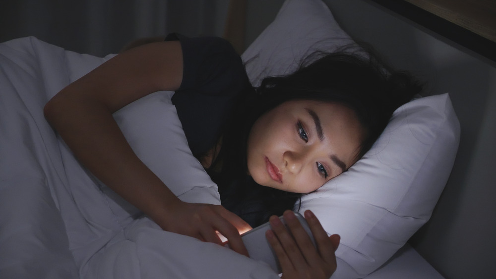 A woman laying in bed and scrolling on her phone