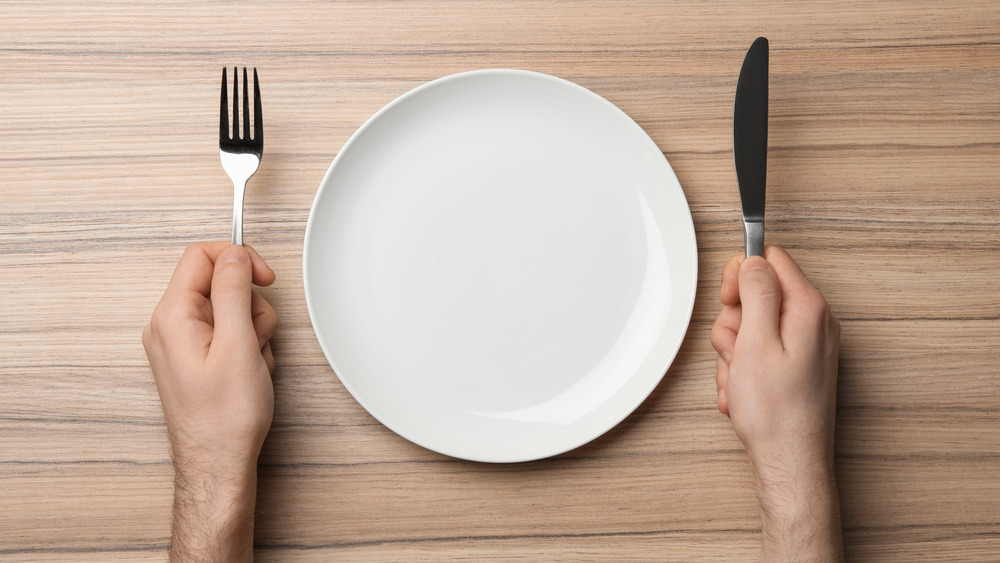 males hands holding a fork and knife with empty plate 