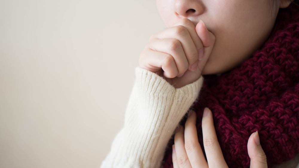 A young woman coughing with a thick scarf around her throat 