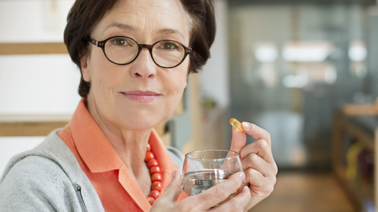 older woman taking a supplement with water