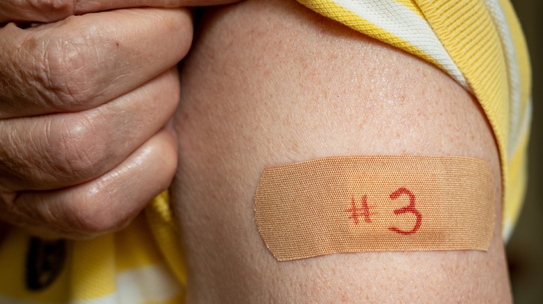Hand pulling up sleeve to reveal bandage labeled "#3" on upper arm