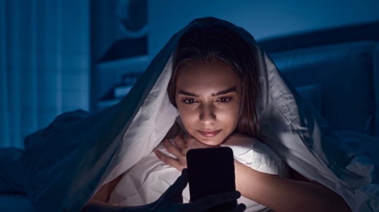 woman looks at phone in bed 