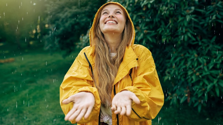 a woman smiling and holding her hands out to the rain