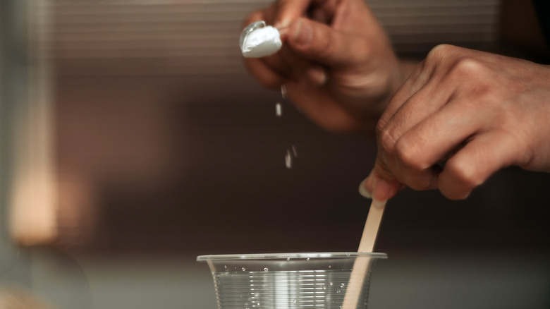 woman's hand pouring baking soda into glass of water