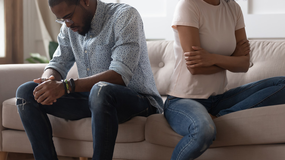 young couple sitting on the couch in an obvious dispute 