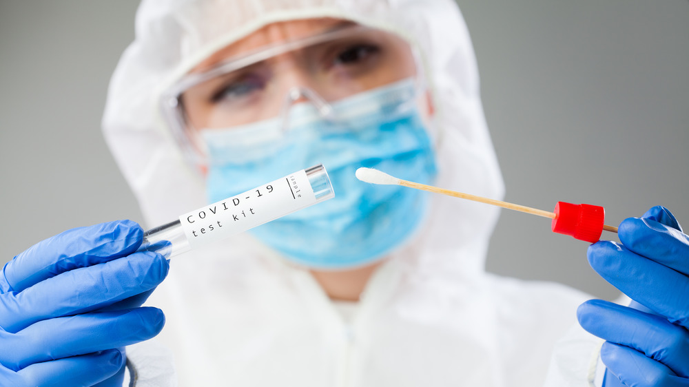 Person in protective suit, googles, and mask holding COVID-19 test swab