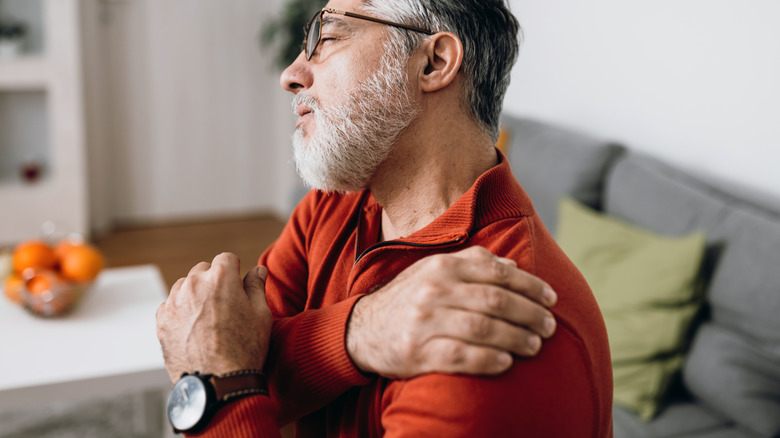 Bespectacled older man rubbing painful shoulder