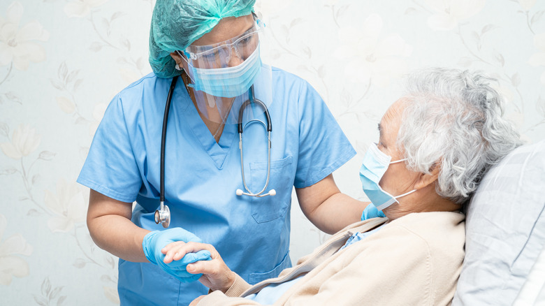 Hospital doctor in PPE holding the hand of elderly masked patient