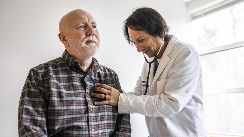 doctor using stethoscope on older man's heart