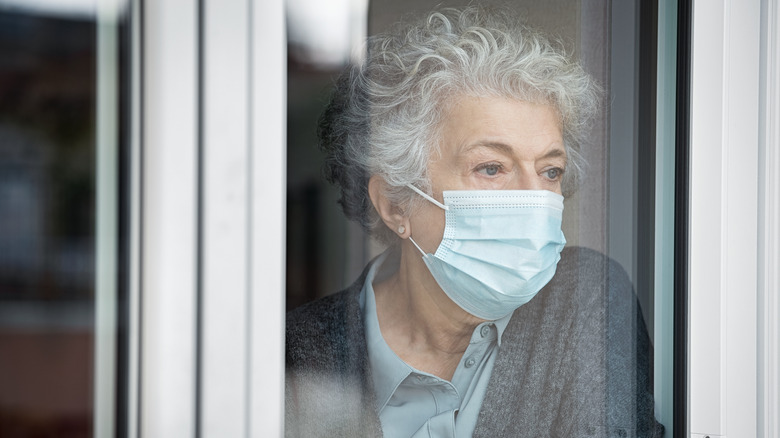 Masked older woman looking out window
