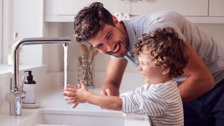 Father watches son washing hands