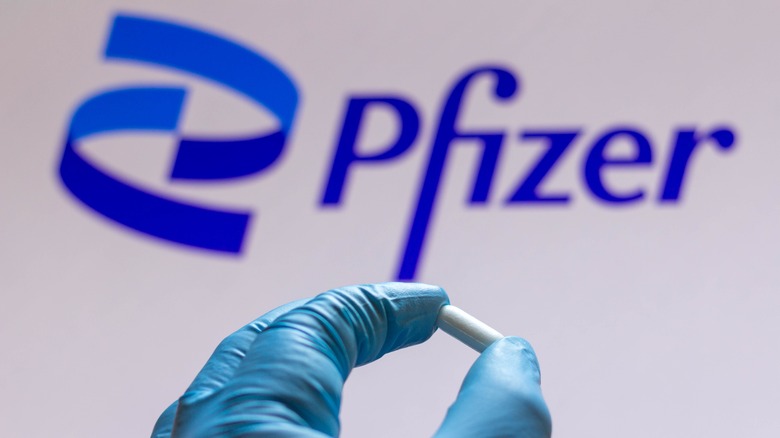 person wearing gloves holding pill in front of Pfizer logo