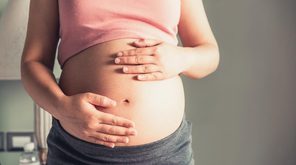 Pregnant woman holding her belly with two hands.