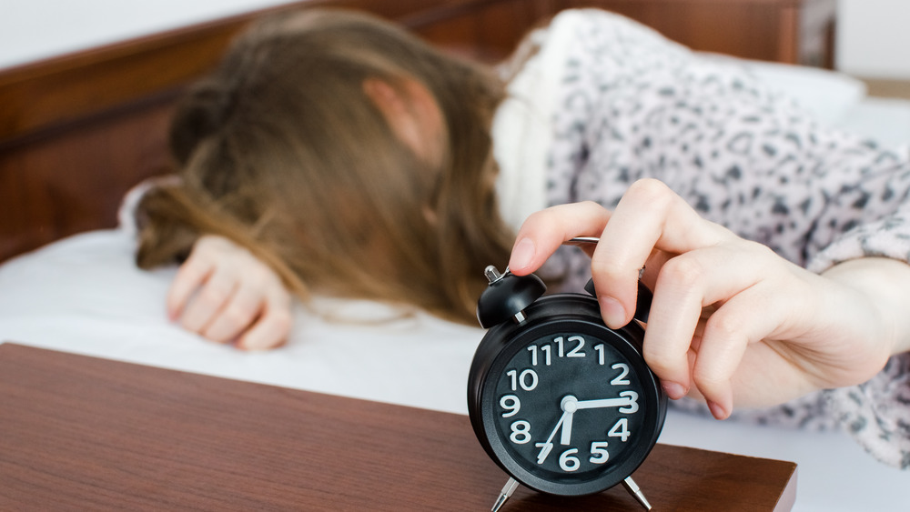 Young woman girl turns off alarm clock waking up in the morning from a call. Unrecognizable student do not want to wake up early for school or univercity. Oversleep, not getting enough sleep concept.