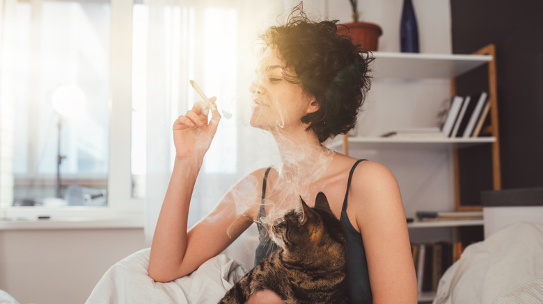 woman holding cat and smoking indoors