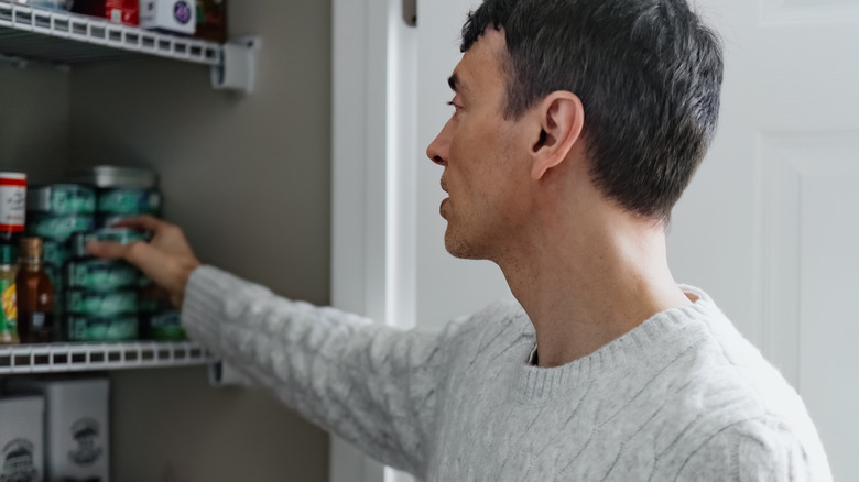 man taking canned tuna out of kitchen pantry