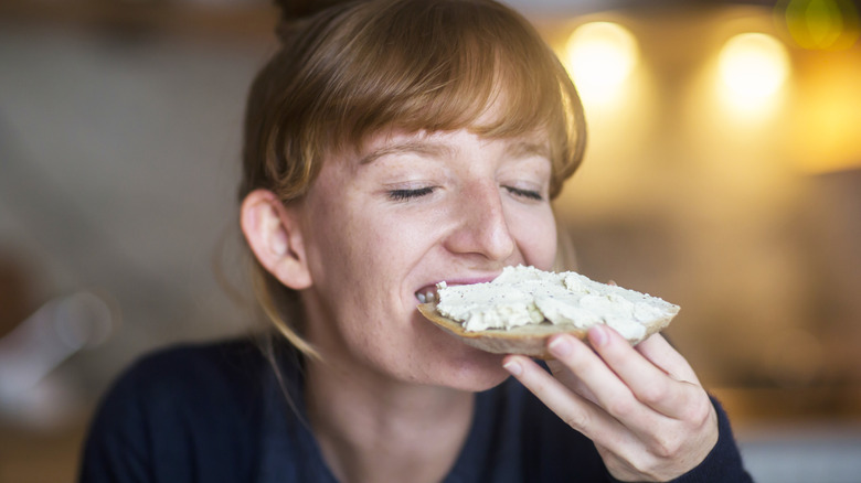 A woman enjoying bread with a cream cheese spread