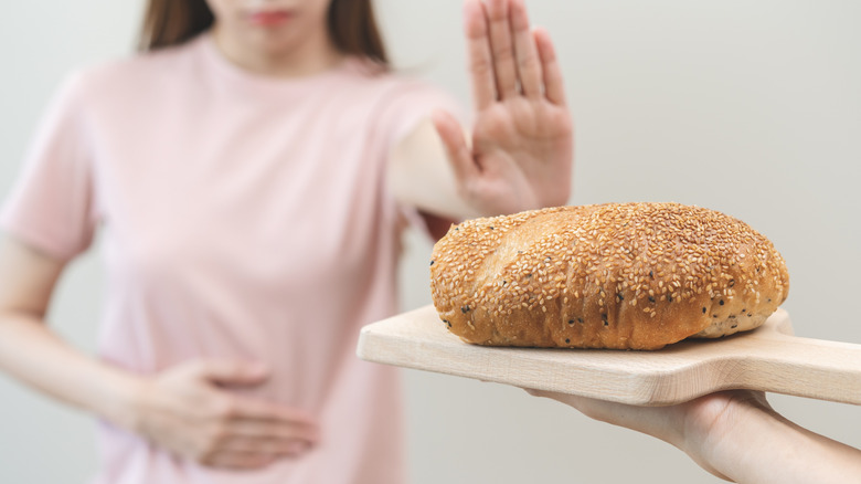 A woman's hand pushing away a loaf of bread while holding her gut