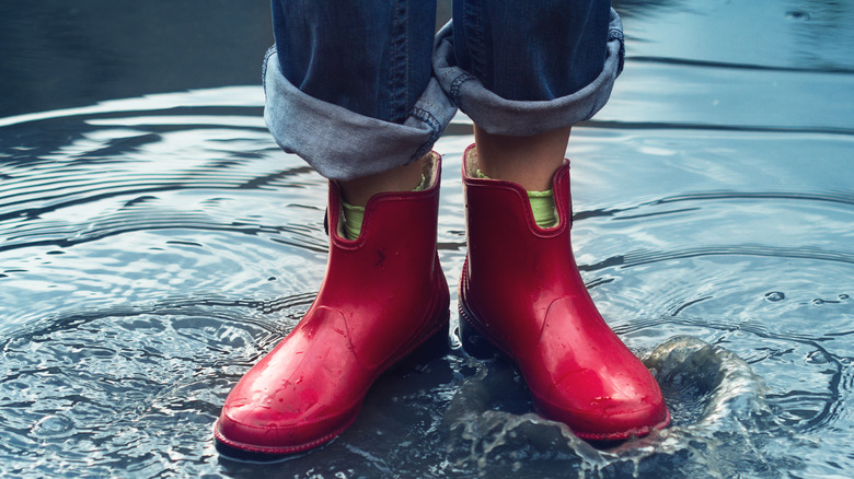 Pair of feet wearing red rain boots standing in puddle