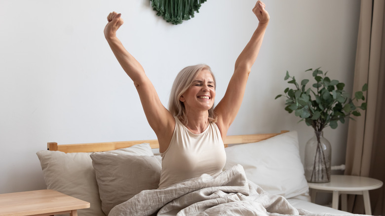 woman raising her arms while sitting up in bed