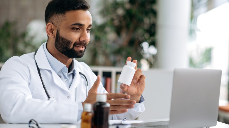 Doctor conducting telehealth appointment holding up a prescription bottle