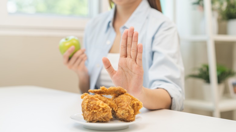 woman waving away fried chicken while holding an apple