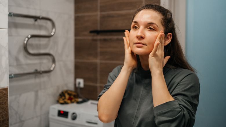 woman looking in mirror and giving self facial massage