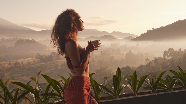 A woman drinking tea while enjoying a sunrise in an exotic location