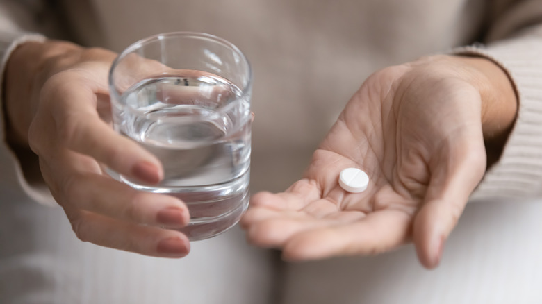 woman holding glass of water with aspirin