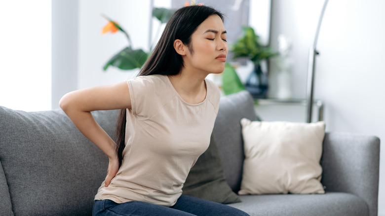 woman with back pain seated on couch
