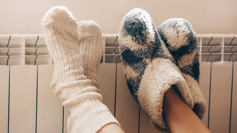 Two pairs of feet wearing fuzzy socks leaning up on a heater