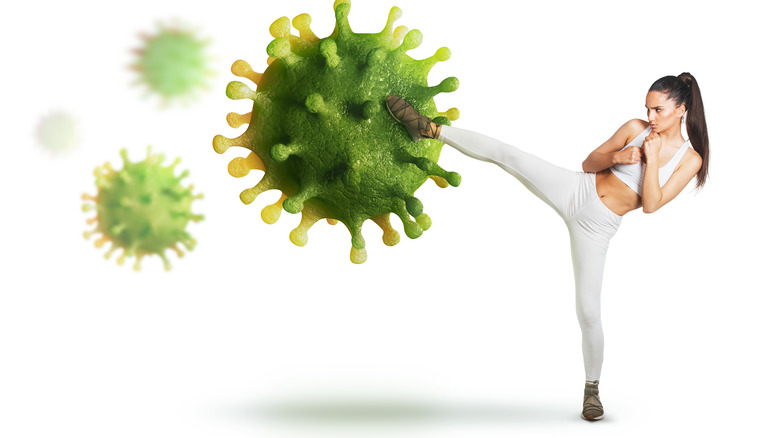 Person in white workout clothes kicking at a large replica of the SARS-CoV-2 virus