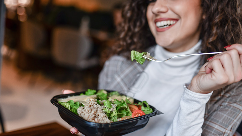smiling woman eating canned tuna fish on salad