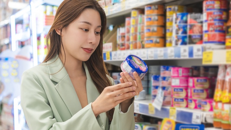 woman examining canned tuna in grocery store