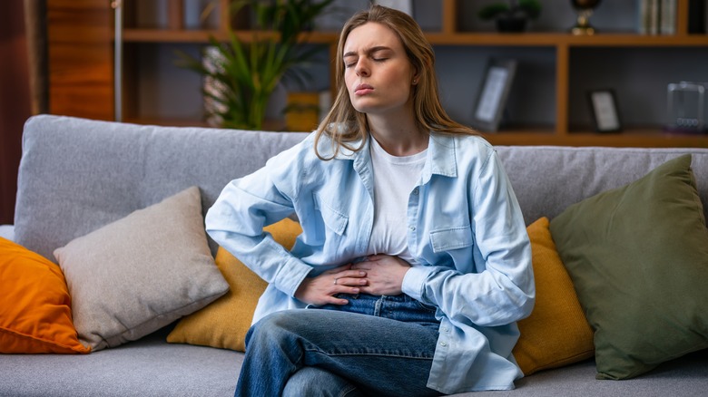 Woman on couch holding stomach in pain