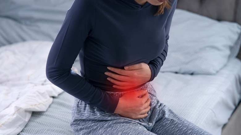 Woman sitting in bed, having stomach pain 