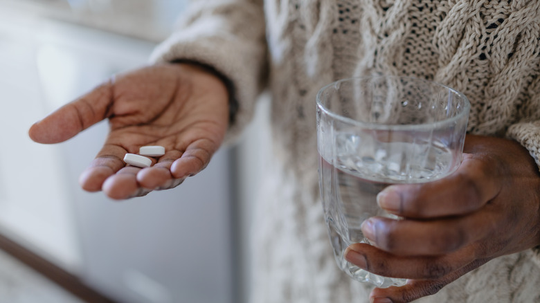 hand holding pills and a glass of water