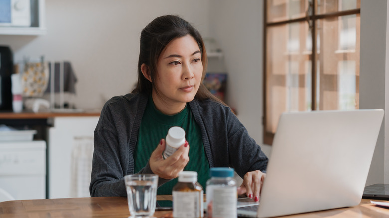 woman holding a medication while looking at her computer