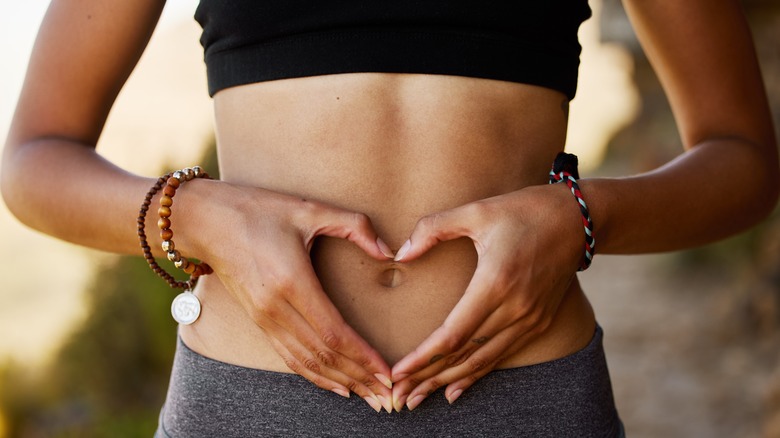 Woman's hands forming heart on bellybutton